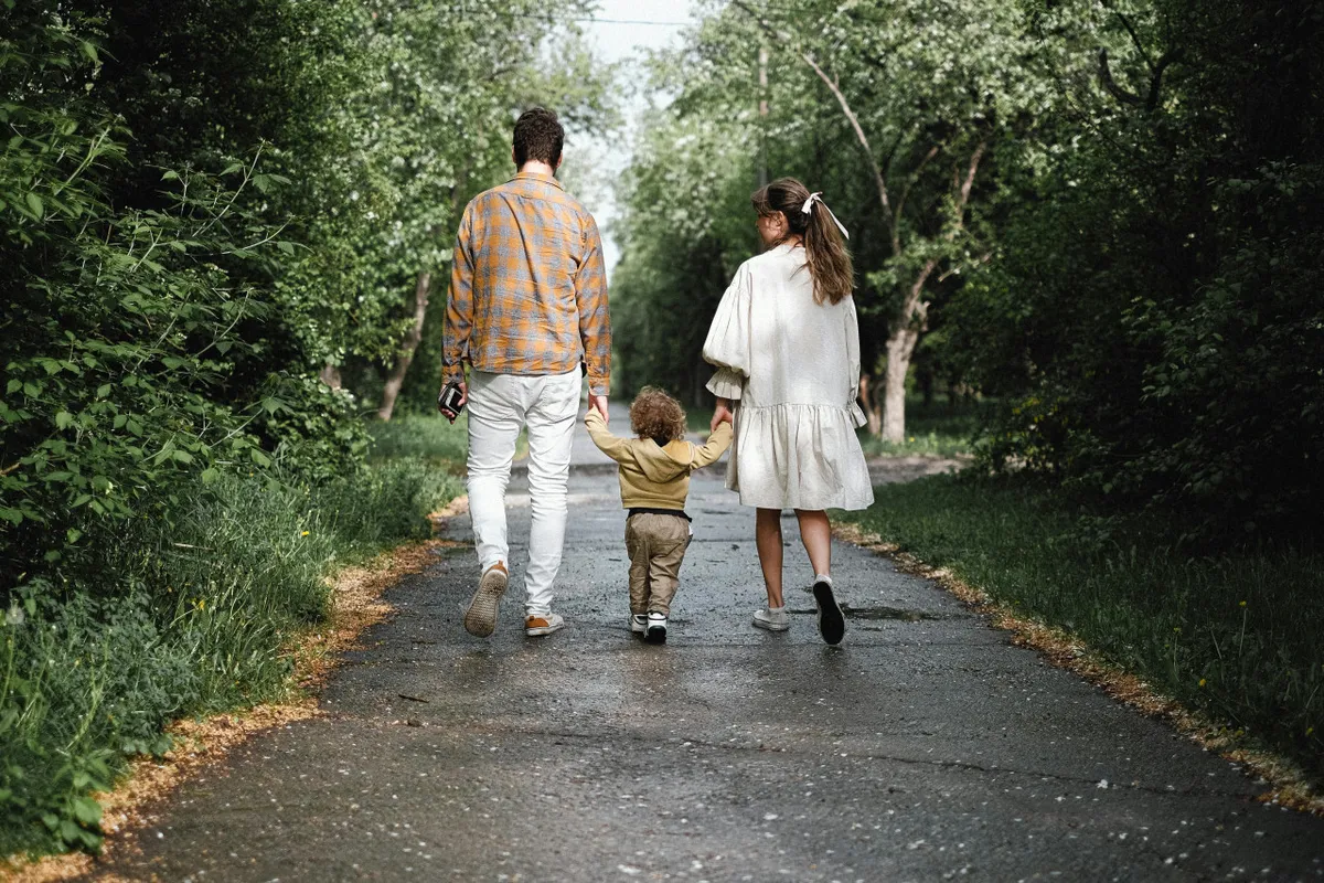 A family is seen walking together along a scenic pathway bordered by lush trees, suggesting easy access to nature and local outdoor adventures. The image conveys a sense of joy, exploration, and togetherness in a natural setting.