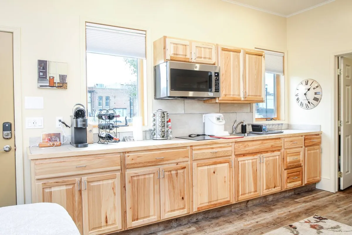 A view of a welcoming kitchen highlighting wooden cabinets, a microwave, and a sunny window that bathes the room in natural light. Countertop appliances and a drip coffee pot are clearly visible, suggesting convenience and the enjoyment of morning rituals.