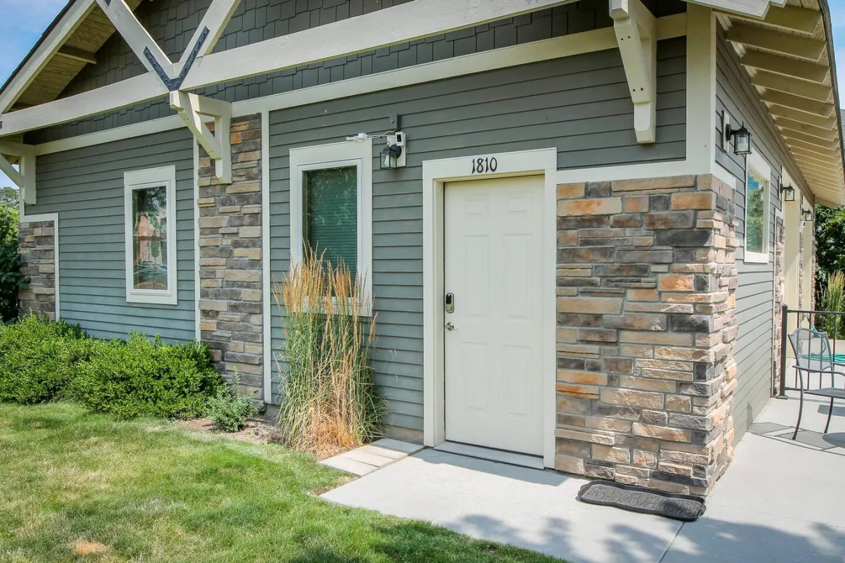 A closer look at the cottage’s entryway, highlighting a welcoming front door framed by stonework, well-kept landscaping, and a peaceful garden area just outside.