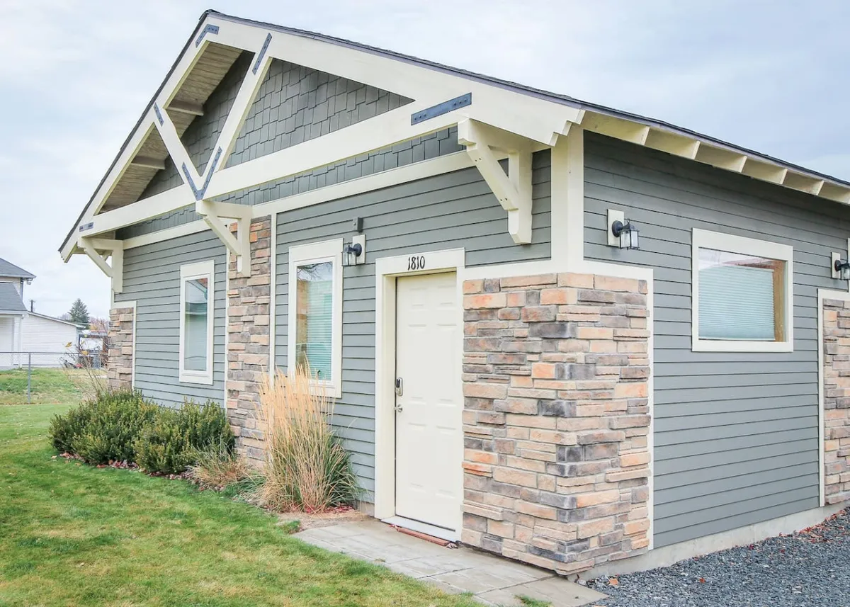 A charming cottage exterior featuring a welcoming front door, attractive stone accents, and a distinctive roofline. The landscaping and small garden area offer a hint of privacy and comfort, while the porch invites guests to relax and soak in the downtown atmosphere.
