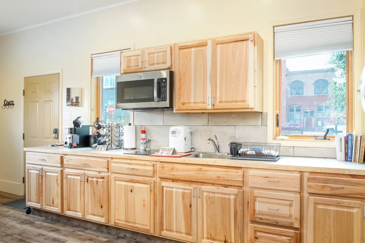A welcoming kitchen scene featuring wooden cabinets, a bright kitchen window, countertop appliances, and a cozy setup ready for cooking and socializing. The layout suggests a space where guests might gather to plan their day or prepare a quick meal before heading out.
