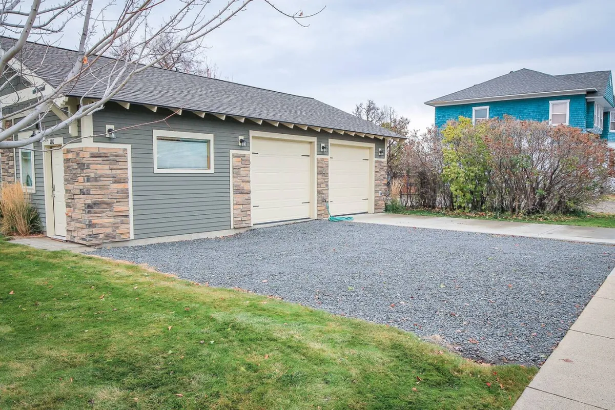 A view of the exterior with garage doors, stone accents, and a wide gravel driveway. The scene conveys a sense of separation from neighbors and an easy, welcoming arrival—key elements for guests looking for privacy with their pets and easy city access.