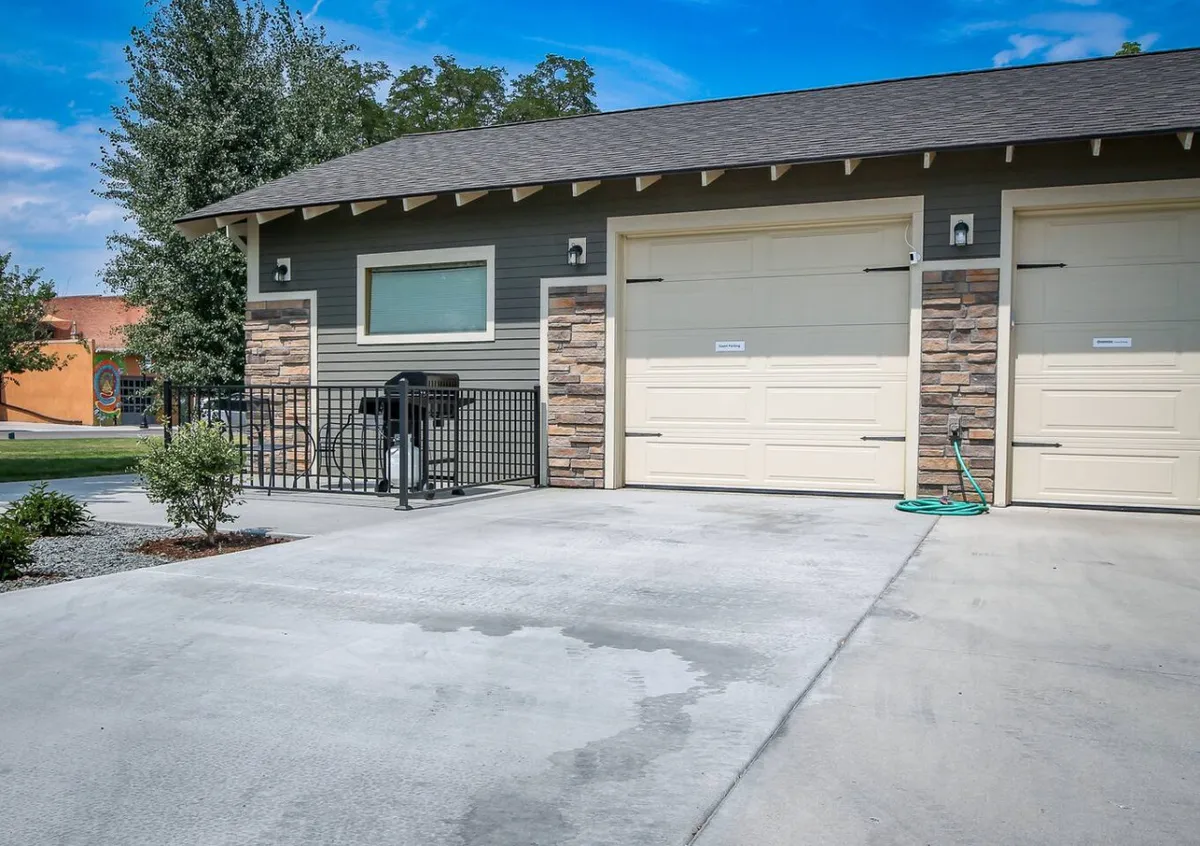 This exterior image shows the inviting patio area beside the garage, with neatly maintained landscaping and ample space for relaxing or gathering outside. The area offers a welcoming, private setting that hints at a stand-alone cottage environment, perfect for guests traveling with pets who need an outdoor space.