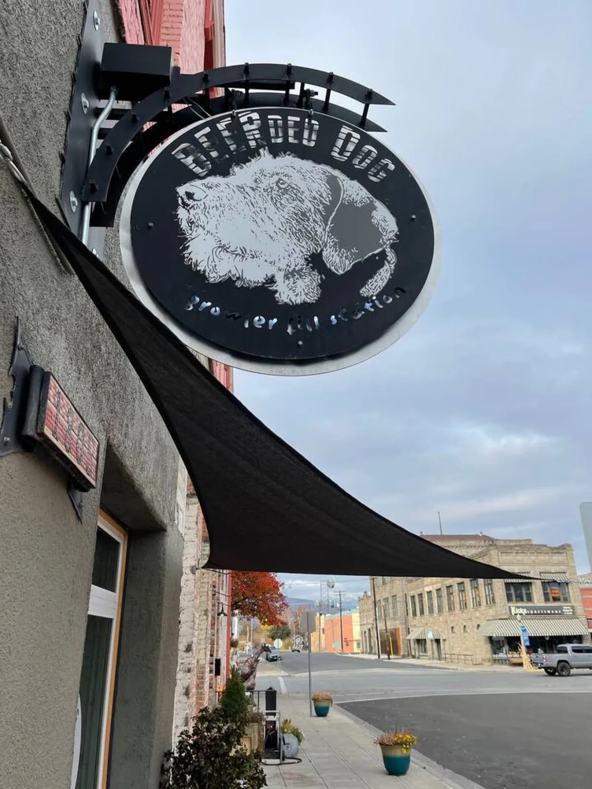 A street-level view of the 'Bearded Dog' with clear signage, a welcoming awning, and glimpses of the street beyond, capturing the local flavor and social spirit of Baker City's downtown establishments.